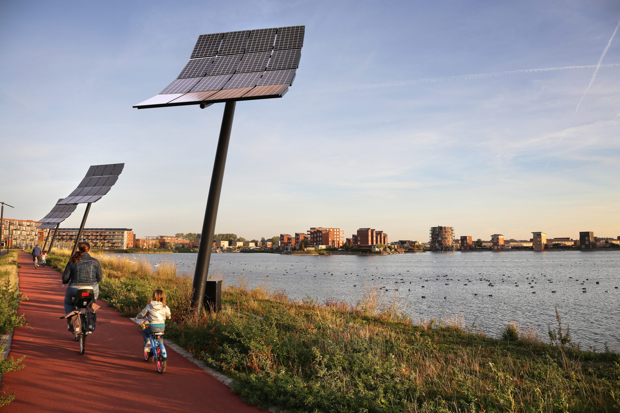 twee personen fietsen langs water, op de achtergrond is een woning zichtbaar